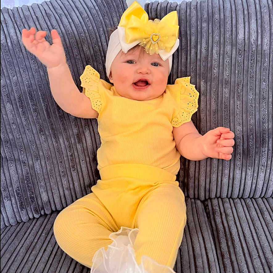 Marliya-Mae is registered to the contest to win money with this photo: baby, baby_girl, bow, child, closeup, couch, cute, fabric, gray_couch, happy, headband, indoor, infant, person, plush, portrait, sitting, smiling, toddler, yellow_clothing