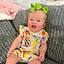 baby, child, smiling, sitting, couch, green_bow, colorful_clothing, floral_pattern, pink_blanket, home_interior, happy, cute, infant, portrait, indoors, person, furniture, cozy, bright, young_child