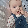 adorable, baby, blanket, blue_eyes, child, close_up, cute, denim_overalls, eyelashes, floral_shirt, hand_in_mouth, heart_pocket, infant, lying_down, playful, portrait, skin, smiling, soft_texture, young