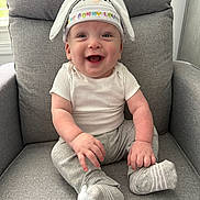 Brodie is registered to the contest to win money with this photo: baby, smile, bunny_hat, sitting, armchair, grey_clothing, infant, happy, cute, indoors, child, sock, face, portrait, young_child, cozy, soft_lighting, comfortable, hat, casual_clothing