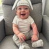 baby, smile, bunny_hat, sitting, armchair, grey_clothing, infant, happy, cute, indoors, child, sock, face, portrait, young_child, cozy, soft_lighting, comfortable, hat, casual_clothing