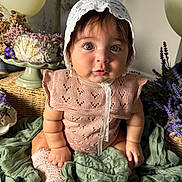 Stella is registered to the contest to win money with this photo: baby, infant, knitted_clothing, bonnet, blue_eyes, curly_hair, sitting, green_fabric, flowers, wicker_basket, soft_lighting, portrait, cute, child, indoor, decor, pastel_colors, sock, plush, closeup