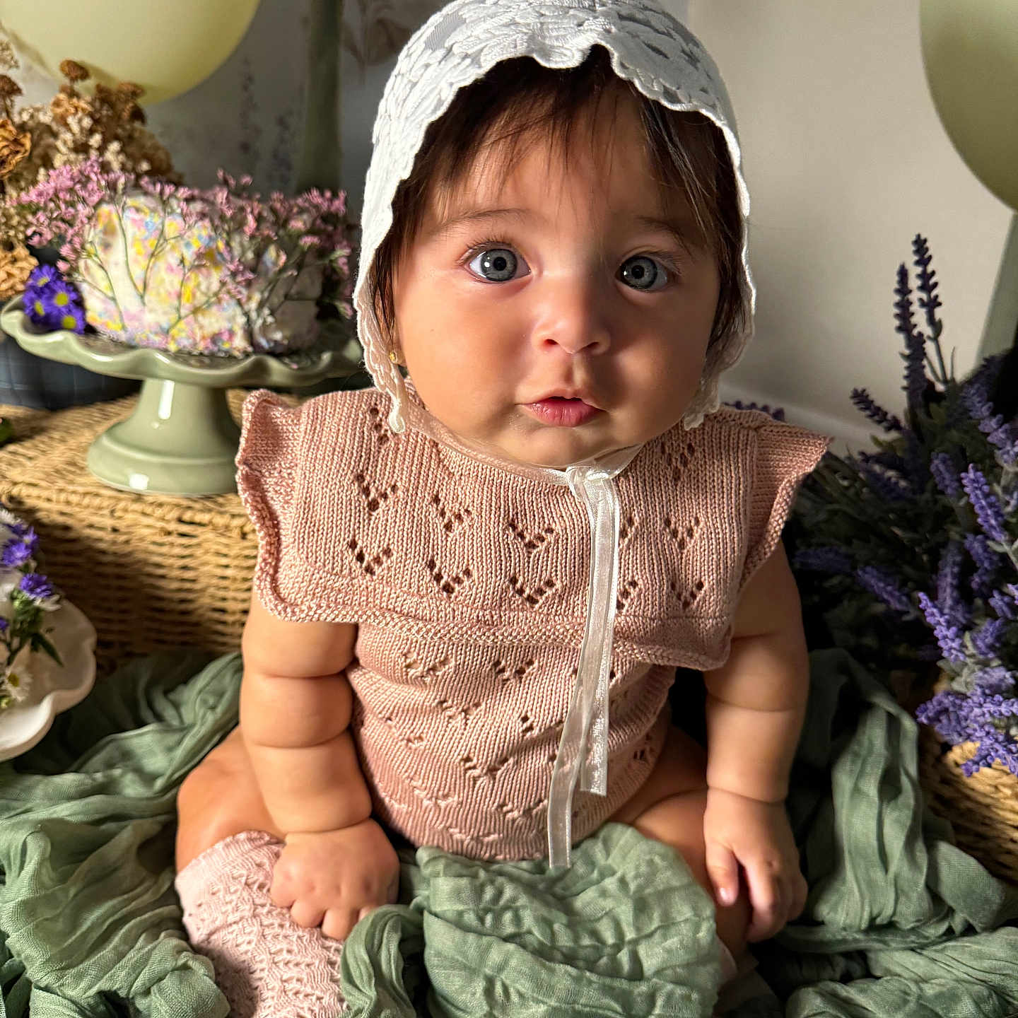 Stella is registered to the contest to win money with this photo: baby, blue_eyes, bonnet, child, closeup, curly_hair, cute, decor, flowers, green_fabric, indoor, infant, knitted_clothing, pastel_colors, plush, portrait, sitting, sock, soft_lighting, wicker_basket