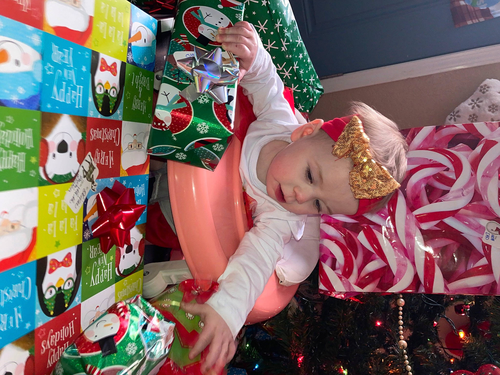 Remington is registered to the contest to win money with this photo: baby_toddler_clothing, carmine, child, christmas, christmas_decoration, christmas_eve, christmas_ornament, christmas_tree, event, fictional_character, fun, green, happy, headwear, holiday, lap, person, present, room, sock