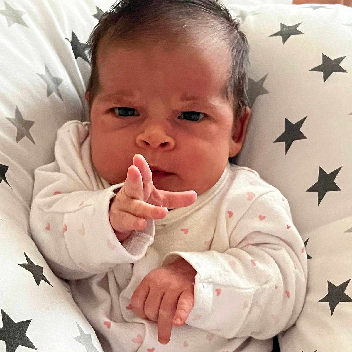 Amelia joined the competition — help win amazing prizes! baby, child, cozy, cushion, cute, expression, face, hands, indoor, infant, newborn, onesie, person, pointing, portrait, serious, sleepwear, small_hands, soft, star_pattern