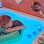balls, bathroom, bathtub, blue_light, child, chrome, curious, faucet, floatation_device, floating, indoor, mirror, orange_wall, person, reflection, safe, toddler, wall, water, young_child