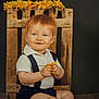 baby, barefoot, child, clothing, cute, decorative, flower, happy, indoors, infant, portrait, red_hair, sitting, smiling, studio, suspenders, white_shirt, wooden_crate, wooden_floor, yellow_flower