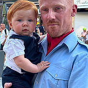 Maélyo participe au concours pour gagner de l'argent avec cette photo : baby, background, casual, child, closeup, clothing, daylight, expression, face, family, holding, infant, man, outdoor, parent, people, portrait, redhead, street, urban