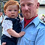 baby, background, casual, child, closeup, clothing, daylight, expression, face, family, holding, infant, man, outdoor, parent, people, portrait, redhead, street, urban