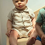 Ambrossio a rejoint le concours — aidez-le/la à gagner de superbes lots ! toddler, child, sitting, wooden_bench, beige_clothing, short_sleeves, shorts, indoor, natural_light, serious_expression, barefoot, person, face, skin, hair, light_shadows, furniture, two_children, casual_wear, young