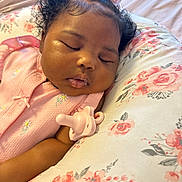 Paisley is registered to the contest to win money with this photo: baby, sleeping, pink_clothing, bow, curly_hair, pacifier, pillow, floral_pattern, infant, peaceful, resting, cute, face, child, indoors, soft_lighting, closeup, skin, head, portrait