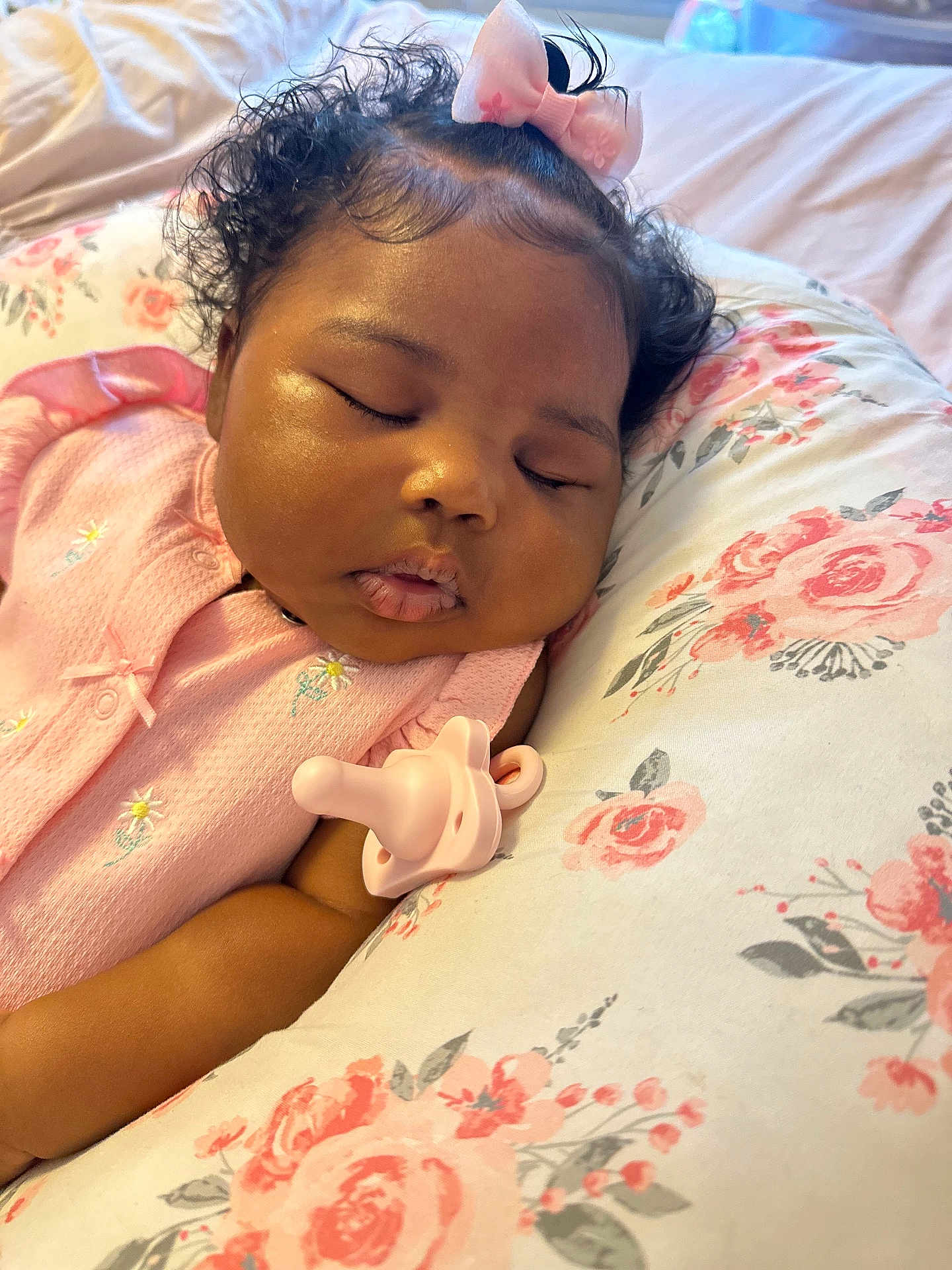 Paisley is registered to the contest to win money with this photo: baby, sleeping, pink_clothing, bow, curly_hair, pacifier, pillow, floral_pattern, infant, peaceful, resting, cute, face, child, indoors, soft_lighting, closeup, skin, head, portrait