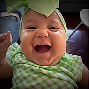 Trinity is registered to the contest to win money with this photo: baby, child, smiling, laughing, headband, bow, green_clothing, chubby_cheeks, portrait, indoor, happy, cute, infant, closeup, person, cheerful, face, toddler, apparel, fashion