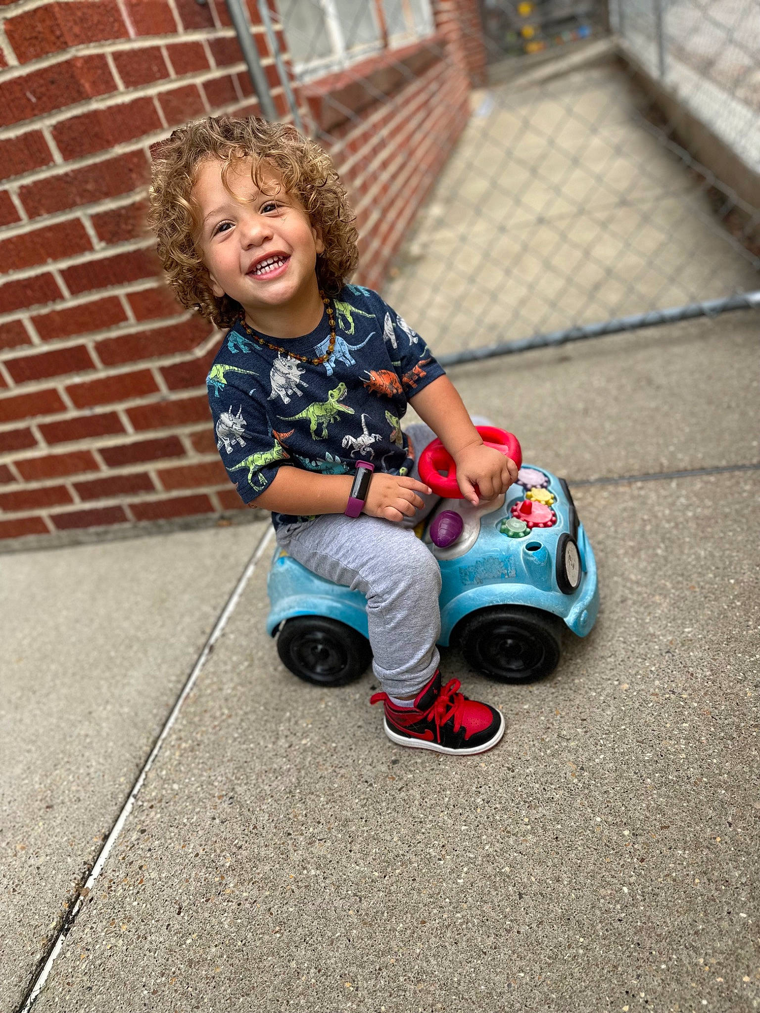 Josiah joined the competition — help win amazing prizes! asphalt, automotive_tire, baby_toddler_clothing, child, face, fun, grass, happy, joy, leisure, person, recreation, riding_toy, road_surface, rolling, sidewalk, sitting, smile, tire, toddler
