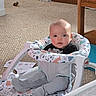baby, baby_seat, baby_toys, carpet, carpeted_floor, child, clothing, curious, cute, face, footwear, furniture, home, indoor, infant, person, rosy_cheeks, sitting, toy, wooden_table
