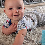 Cory is registered to the contest to win money with this photo: baby, infant, smile, face, hand, carpet, floor, mickey_mouse, clothing, toddler, cute, indoor, baby_gate, playful, happy, person, skin, head, lying, expression