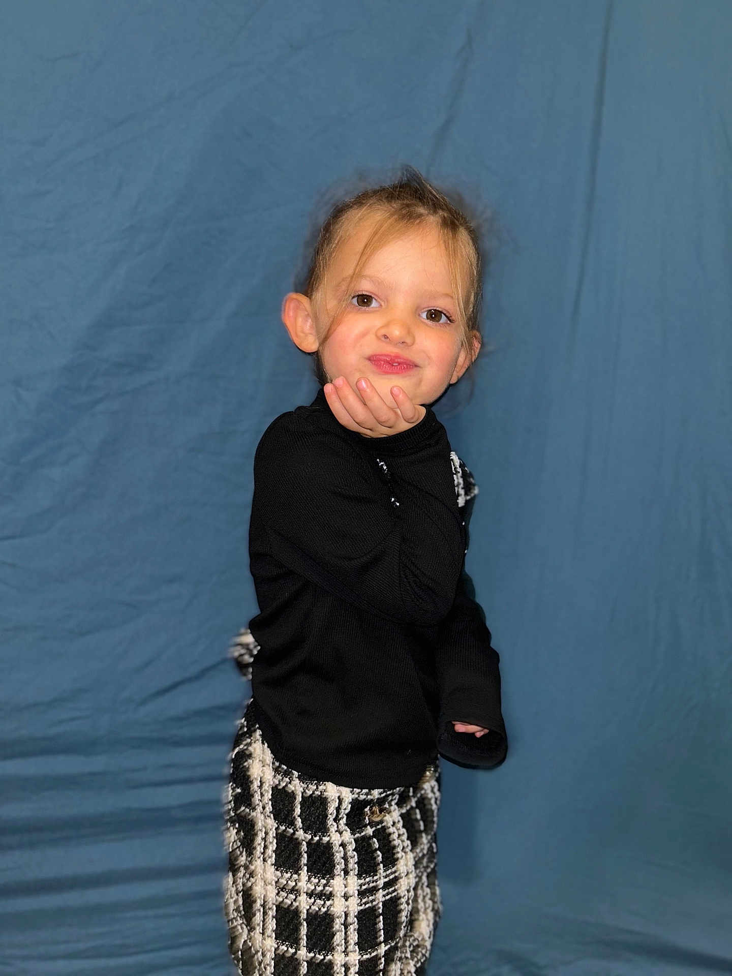 Celeste a rejoint le concours — aidez-le/la à gagner de superbes lots ! child, toddler, girl, portrait, blue_background, black_top, plaid_skirt, hand_on_face, playful_pose, smiling, blonde_hair, ponytail, ears_visible, indoor, studio_style, fashion, eyes, cute, candid, portrait_photography