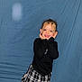 black_top, blue_backdrop, candid, checkered_skirt, child, fashionable, flash, girl, hands_on_cheeks, happy, indoor, playful, portrait, posing, single_person, smiling_child, studio_style, tooth_gap, wrinkled_sheet, young_child