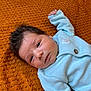 baby, infant, face, hair, blue_sweater, button, blanket, orange, texture, lying_down, portrait, cute, child, young, skin, expression, hand, cozy, warm, indoors