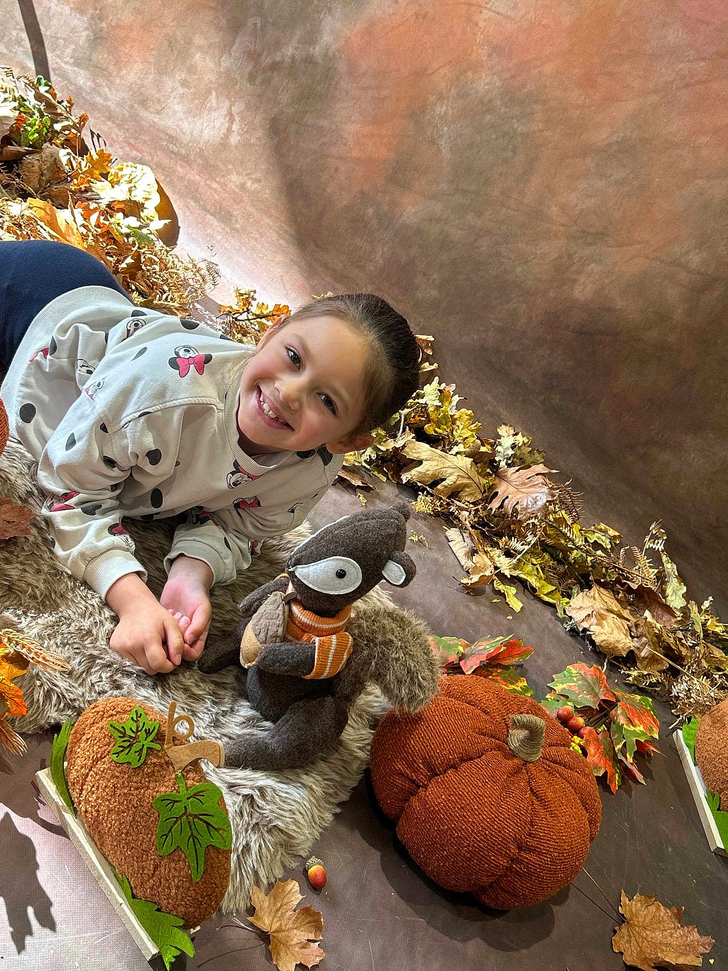 Kayla a rejoint le concours — aidez-le/la à gagner de superbes lots ! child, girl, smile, portrait, plush_squirrel, stuffed_animal, pumpkin, knitted_pumpkin, autumn_leaves, fall_decor, cozy, fur_rug, happy, indoor, seasonal_props, playful, smiling_face, costume_props, fabric, photography