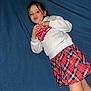 bed, blue_sheet, casual_clothing, child, face, flash_photo, girl, hands, indoor, legs, long_hair, lying_down, plaid_skirt, playful, portrait, pout, red, sweatshirt, white, young_child