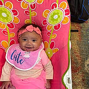 Harmani is registered to the contest to win money with this photo: accessory, baby, baby_seat, backpack, bib, carpet, child, clothing, cute, floral_pattern, happy, headband, indoor, infant, person, pink_clothing, portrait, sitting, smiling, toddler