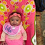accessory, baby, baby_seat, backpack, bib, carpet, child, clothing, cute, floral_pattern, happy, headband, indoor, infant, person, pink_clothing, portrait, sitting, smiling, toddler