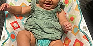 Harmani joined the competition — help win amazing prizes! arms, baby, baby_seat, child, colorful, cute, face, green_dress, happy, indoor, infant, joyful, legs, patterned, person, playful, portrait, seated, smiling, socks