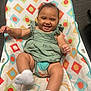 arms, baby, baby_seat, child, colorful, cute, face, green_dress, happy, indoor, infant, joyful, legs, patterned, person, playful, portrait, seated, smiling, socks