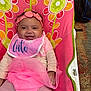 Harmani is registered to the contest to win money with this photo: baby, bib, chair, cheerful, child, clothing, colorful, cute, fabric, face, flower_pattern, happy, headband, indoors, infant, pink, portrait, sitting, smiling, toddler