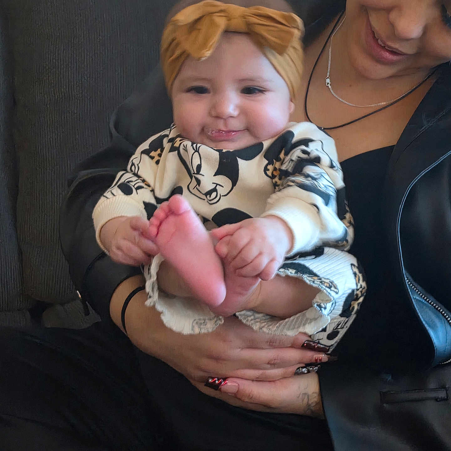 Ximena joined the competition — help win amazing prizes! baby, child, woman, headband, mickey_mouse, clothing, couch, smile, happy, holding, indoor, portrait, person, black_jacket, hand, foot, cute, infant, casual, seated