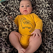 Malakai is registered to the contest to win money with this photo: baby, infant, yellow_onesie, dinosaur_print, blanket, fuzzy_texture, leopard_print, child, cute, lying_down, soft_lighting, indoor, skin, face, legs, hand, foot, cozy, curious_expression, comfortable
