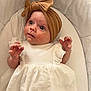 baby, infant, headwrap, bow, white_dress, curious, wide_eyes, soft_cushion, indoor, portrait, child, cute, young, small_hands, looking_up, fabric_texture, wrapped_head, comfortable, closeup, adorable