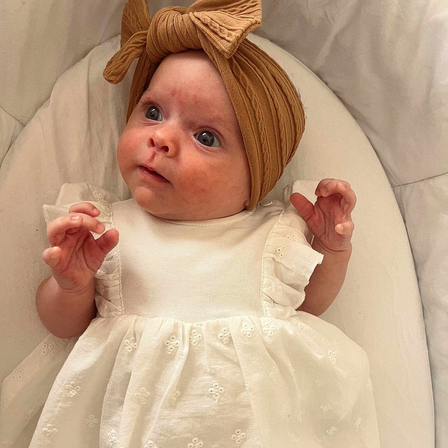 Mya participe au concours pour gagner de l'argent avec cette photo : adorable, baby, bow, child, closeup, comfortable, curious, cute, fabric_texture, headwrap, indoor, infant, looking_up, portrait, small_hands, soft_cushion, white_dress, wide_eyes, wrapped_head, young