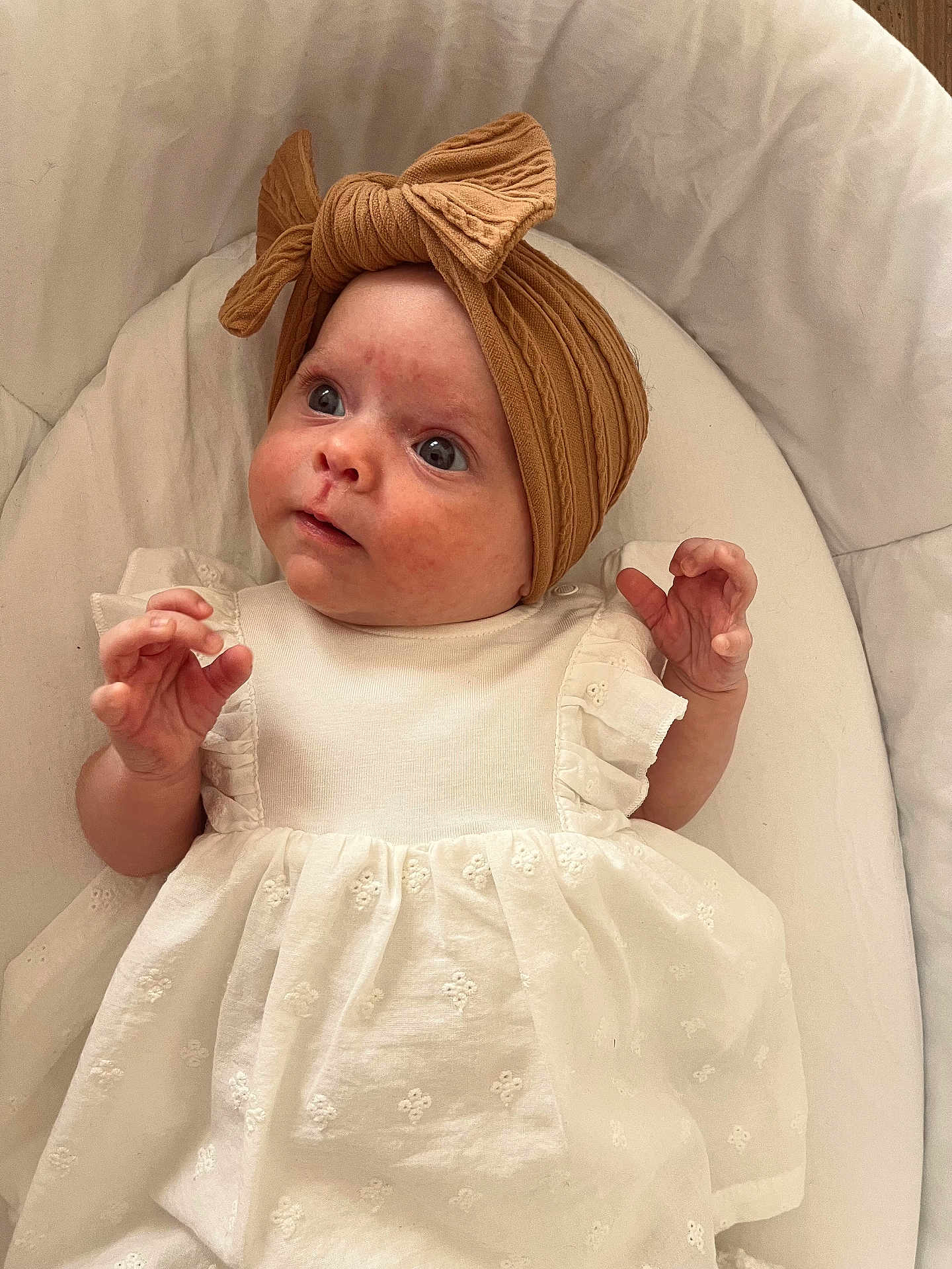 Mya participe au concours pour gagner de l'argent avec cette photo : baby, infant, headwrap, bow, white_dress, curious, wide_eyes, soft_cushion, indoor, portrait, child, cute, young, small_hands, looking_up, fabric_texture, wrapped_head, comfortable, closeup, adorable