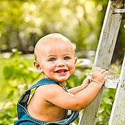 Lex is registered to the contest to win money with this photo: baby, child, denim_overalls, smiling, blue_eyes, toothy_grin, ladder, outdoor, greenery, sunlight, bokeh, grass, nature, cute, happy, skin, arm, face, portrait, one_strap