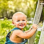 baby, child, denim_overalls, smiling, blue_eyes, toothy_grin, ladder, outdoor, greenery, sunlight, bokeh, grass, nature, cute, happy, skin, arm, face, portrait, one_strap