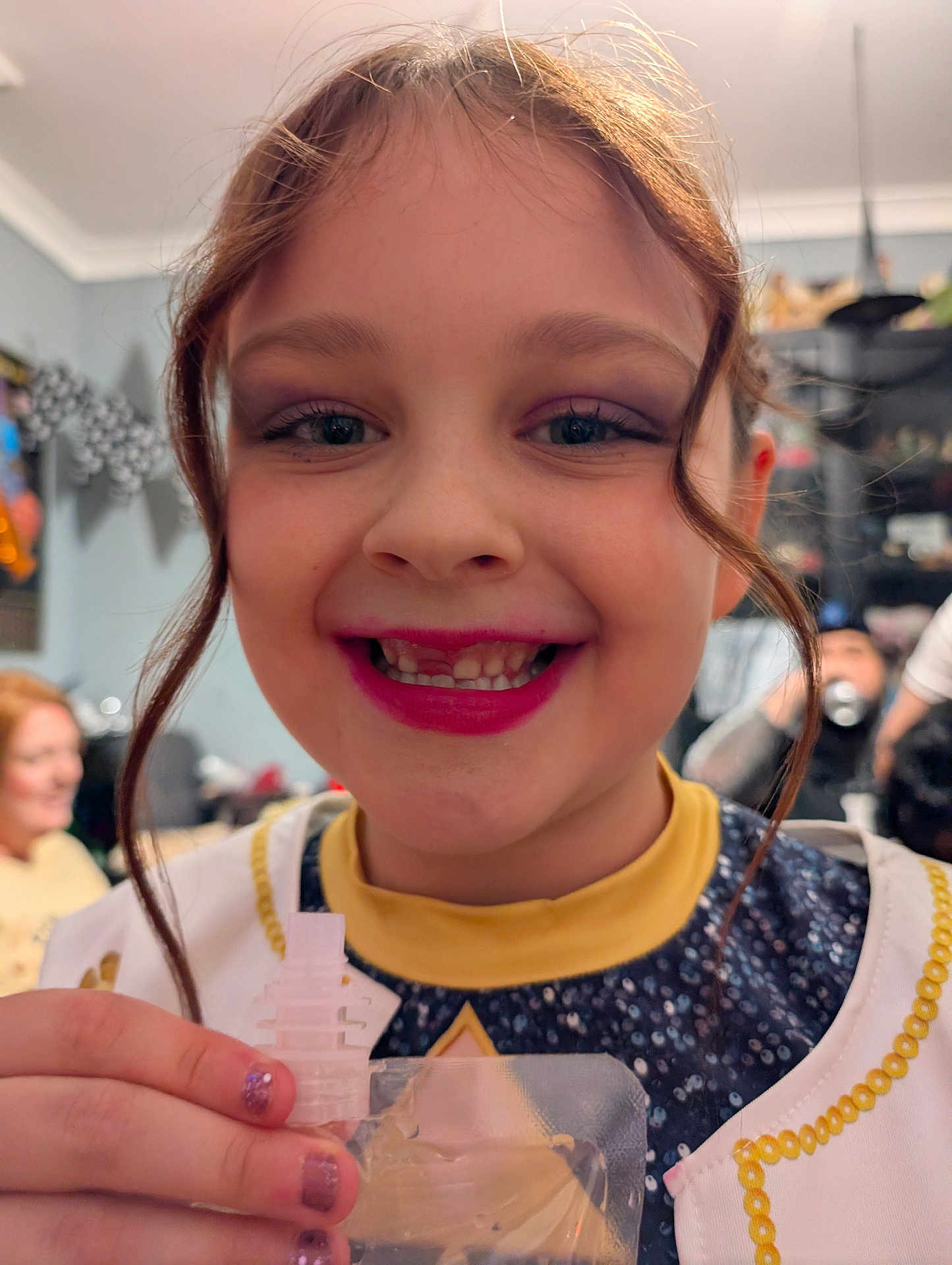 Daisy-May joined the competition — help win amazing prizes! child, girl, smiling, face, makeup, lipstick, hand, snack, pouch, nail_polish, indoor, people, background, hair, clothing, yellow, blue, decorations, happy, portrait