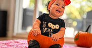Liliana joined the competition — help win amazing prizes! baby, child, infant, portrait, smiling, happy, pumpkin, halloween, autumn, orange_bow, headband, black_shirt, sitting, indoor, window, natural_light, blanket, seasonal, festive, photography