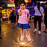 Jasmine Kaur is registered to the contest to win money with this photo: child, girl, portrait, standing, night, neon_lights, festive, outdoor, entertainment_venue, crowd, street, colorful, smiling, fist_bump, pink_shirt, denim_skirt, sneakers, glowing_effect, reflection, city_lights
