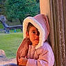 child, toddler, portrait, pink_coat, winter_clothing, hood, fluffy_trim, doorway, window, outdoor, garden, grass, trees, wood, sunlight, sitting, standing, face, smartphone_screenshot, home_screen