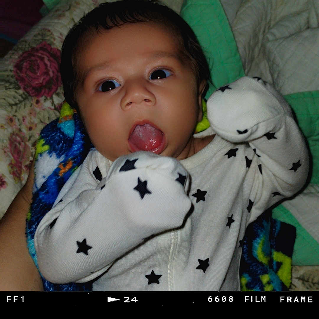 Emiliano joined the competition — help win amazing prizes! baby, infant, face, tongue, onesie, stars, blanket, quilt, bed, raised_hands, expression, cute, child, sleepwear, portrait, indoor, closeup, newborn, person, fabric