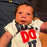 Emiliano joined the competition — help win amazing prizes! baby, infant, child, person, clothing, shirt, text, indoor, portrait, cute, face, eyes, hand, sitting, expression, young, human, toddler, white_shirt, bold_text