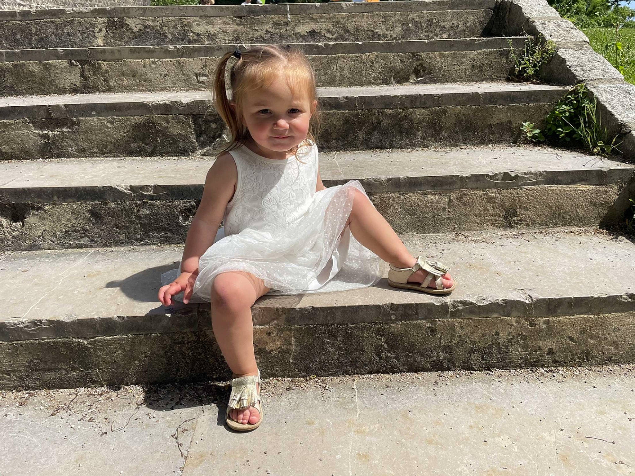 Maëlia a rejoint le concours — aidez-le/la à gagner de superbes lots ! child, day_dress, dress, foot, fun, grass, happy, human_leg, landscape, leisure, pattern, people_in_nature, person, plant, recreation, road_surface, sandal, sitting, smile, stairs