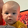 Hugo participe au concours pour gagner de l'argent avec cette photo : baby, child, face, person, portrait, curious, eyes, expression, skin, head, ear, clothing, mustard_shirt, holding, indoor, close_up, adult_arm, background, warm_colors, human