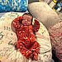 newborn, baby, sleeping, onesie, orange_clothing, animal_print, pillow, text_print, blanket, bed, cozy, indoor, infant, peaceful, resting, soft_furniture, cute, child, portrait, comfort