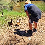 Elias is registered to the contest to win money with this photo: bending, blue_sky, boy, bushes, child, daylight, ducks, grass, nature, outdoor, pond, rocks, shadow, shoes, shorts, sunlight, trees, tshirt, water, wildlife