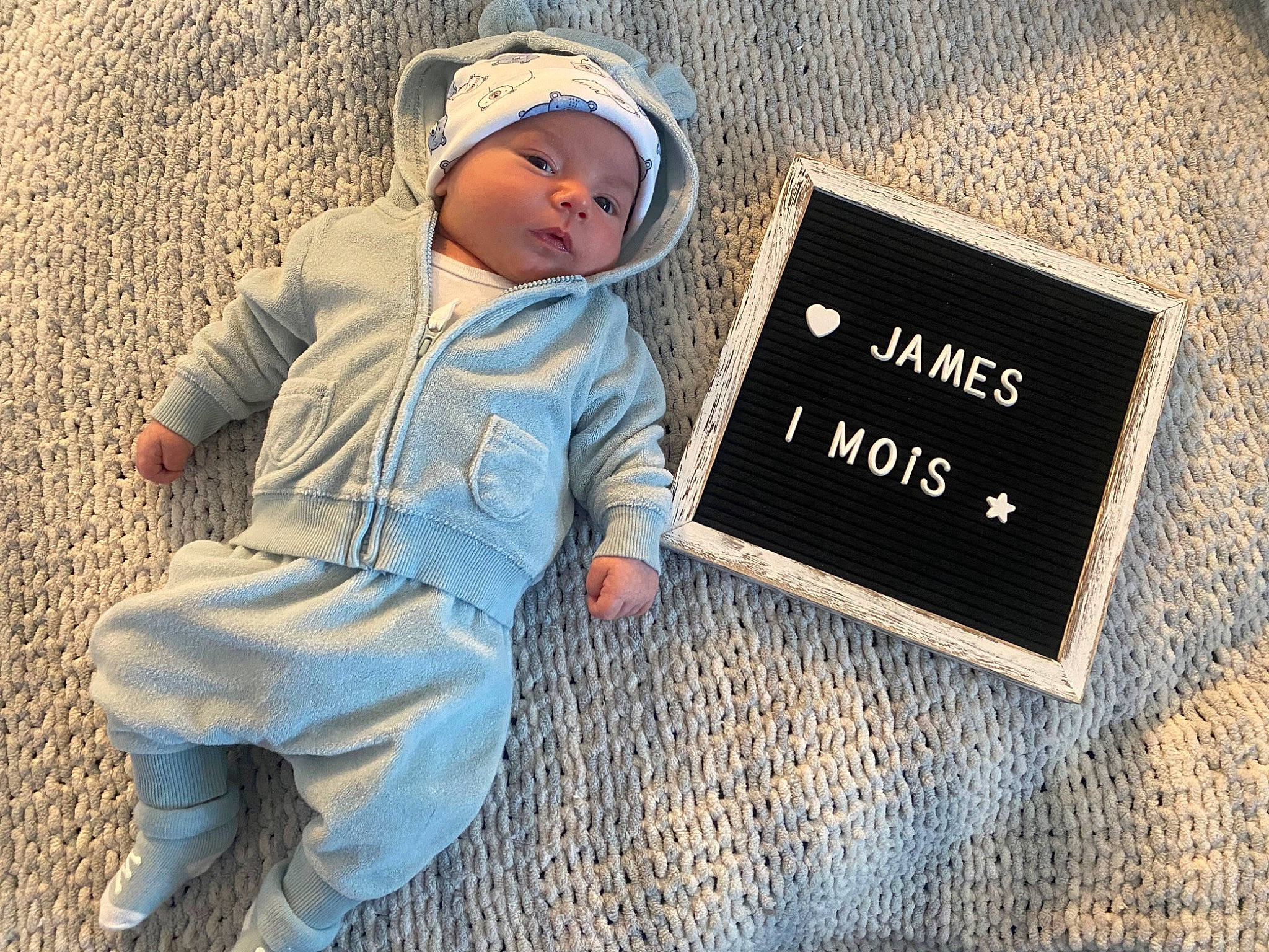 James participe au concours pour gagner de l'argent avec cette photo : baby, baby_toddler_clothing, brand, cap, child, denim, electric_blue, fashion_accessory, flooring, font, grass, happy, headwear, landscape, logo, outerwear, person, shadow, sitting, sleeve