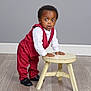 Alan joined the competition — help win amazing prizes! toddler, child, red_suit, white_shirt, stool, wooden_floor, grey_wall, shoes, standing, surprised_expression, indoor, portrait, young_child, curly_hair, fashion, studio, furniture, hands_on_stool, casual_pose, person