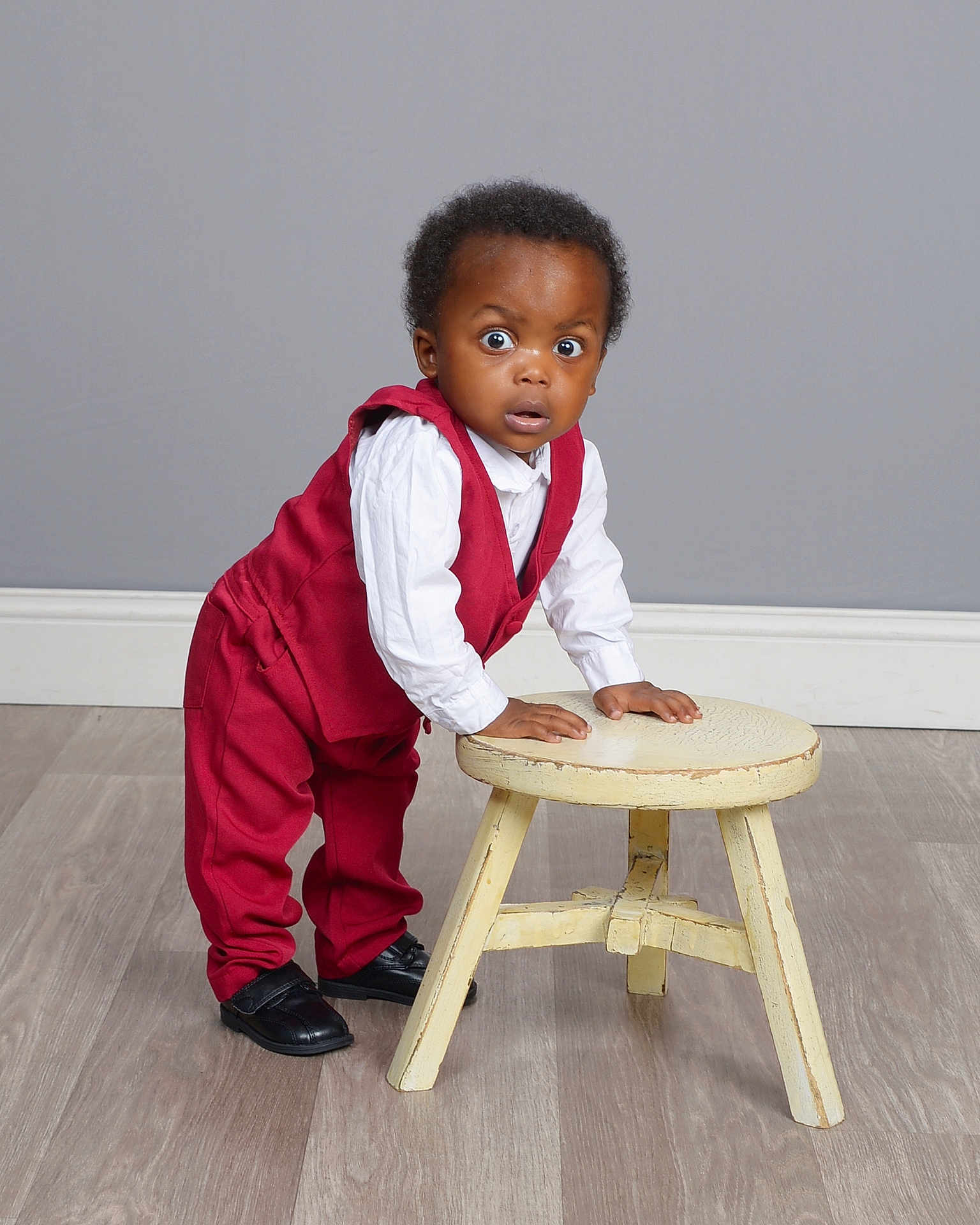 Alan joined the competition — help win amazing prizes! toddler, child, red_suit, white_shirt, stool, wooden_floor, grey_wall, shoes, standing, surprised_expression, indoor, portrait, young_child, curly_hair, fashion, studio, furniture, hands_on_stool, casual_pose, person